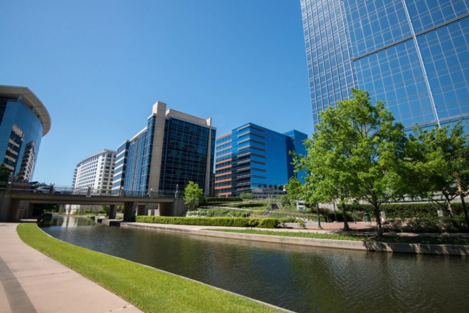 Modern office buildings along a waterway with trees on a clear day in The Woodlands, TX