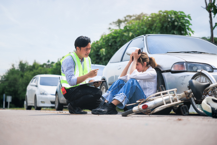 Accident, crash or collision of auto car, bicycle at outdoor. Include asian people i.e. insurance officer man to examining, write document report and young girl or bicycle rider to injury on road. Concept for vehicle crash, insurance claim, emergency and safety.
