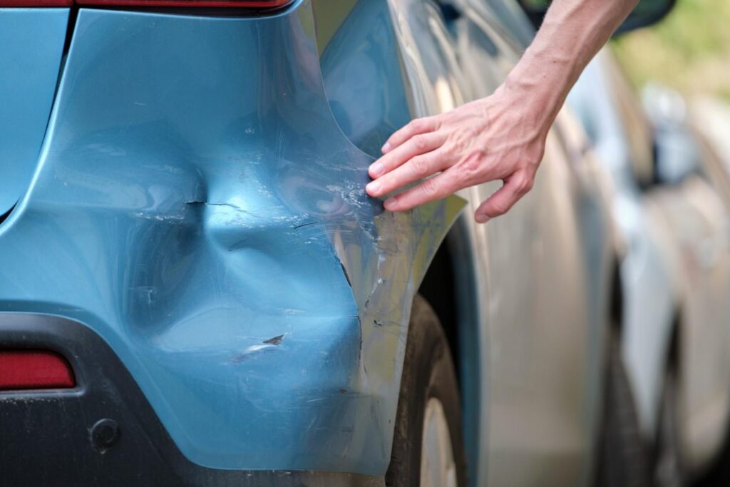 Close view of damaged car rear bumper with visible dent after hit and run accident on street in Bellaire, TX